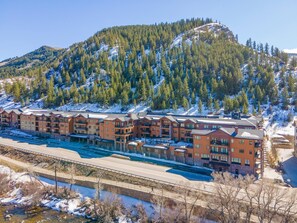 Ein mehrstöckiges Hotel mit Balkonen, im Hintergrund eine Skipiste und im Vordergrund ein Fluss.