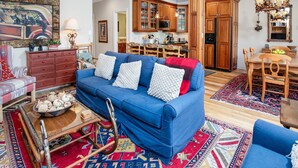A living room with a blue sofa, wooden cabinets, a dining area, and a kitchen. - Sun Vail 23a, 2BD Condo With Vail Mountain Views (Vail)
