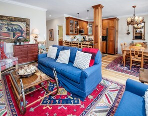 Ein Wohnzimmer mit blauem Sofa, Holzschränken, einem Essbereich und einer Küche.