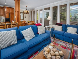 Ein Wohnzimmer mit blauen Sofas, ein Essbereich mit Holzsesseln und eine Küche mit Holzschränken.