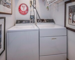 Eine Waschmaschine und ein Trockner in einem Gerät mit Bedienfeld, Abluftschlauch und einem an der Wand befestigten runden Schild mit Text.