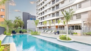 A swimming pool with lounge chairs, surrounded by greenery and modern buildings. - Aconchego Teodoro (São Paulo)