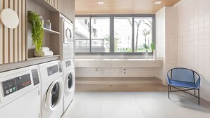 A modern laundry room with a washing machine, dryer, and a large window providing a view of the outside. - Aconchego Teodoro (São Paulo)