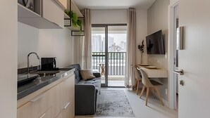 A modern kitchen with a built-in oven, a dining area with a table and chairs, a sofa, and a balcony with a view of the city. - Aconchego Teodoro (São Paulo)
