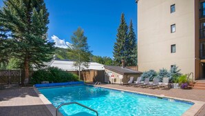Piscina con una escalera metálica, rodeada de sillas de descanso y una valla de madera.