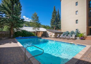A swimming pool with a metal ladder, surrounded by lounge chairs and a wooden fence. - Vail International 111, 2 BD Lionshead Village Condo (Vail)