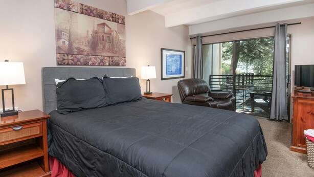 Una habitación de hotel con una cama grande, dos mesitas de noche con lámparas, una silla, un televisor y un balcón con vistas.