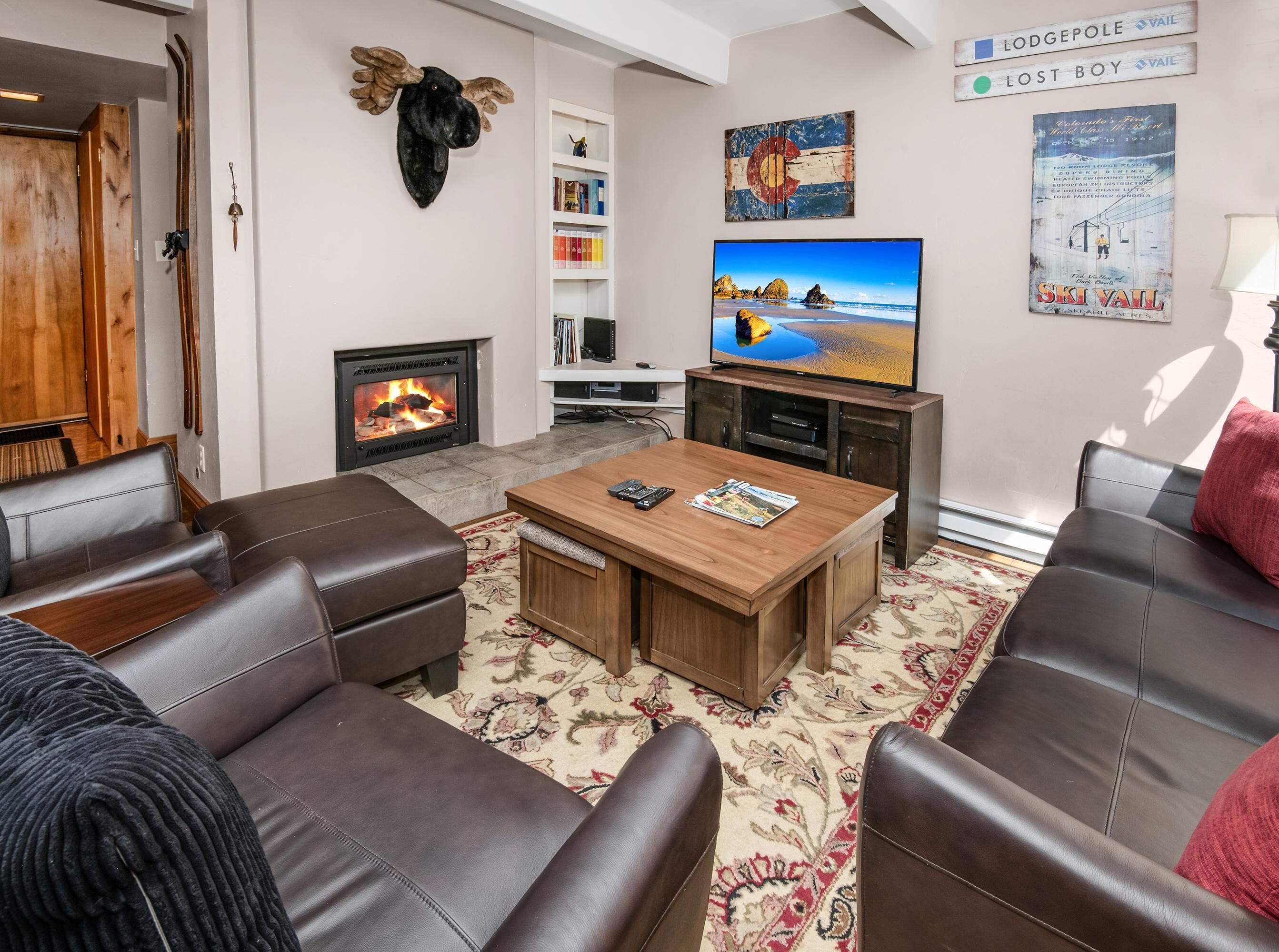 Ein Wohnzimmer mit Ledersofas, einem Holztisch, einem Kamin, einem Fernseher und einem Bücherregal.