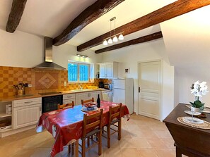 Une cuisine équipée d’une table à manger, de chaises, d’un réfrigérateur et d’une fenêtre avec des rideaux.