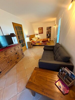 Ein Wohnzimmer mit Sofa, Fernseher, Holzschrank, Bett mit Steppdecke und Bücherregal.