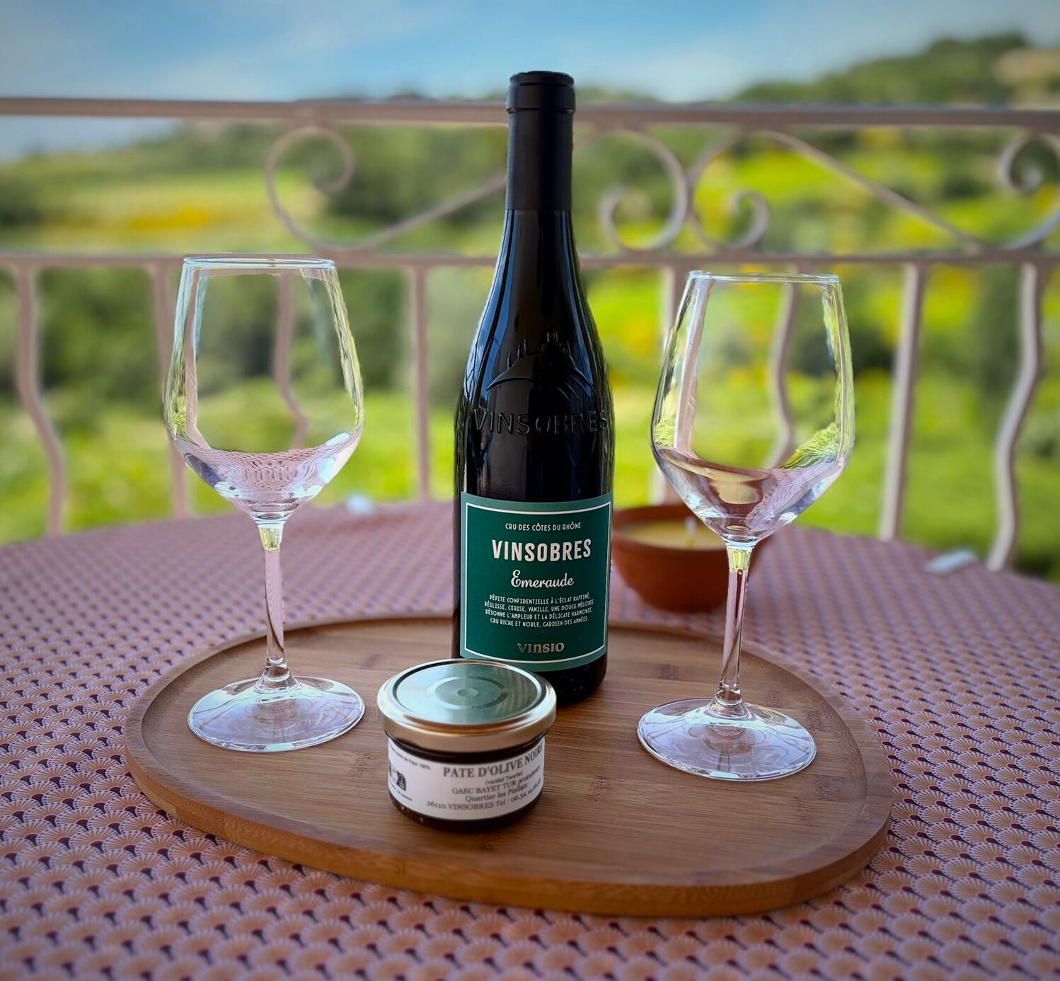 Una botella de vino Vinsobres, dos copas de vino vacías y un tarro pequeño de paté de aceitunas sobre una tabla de madera.
