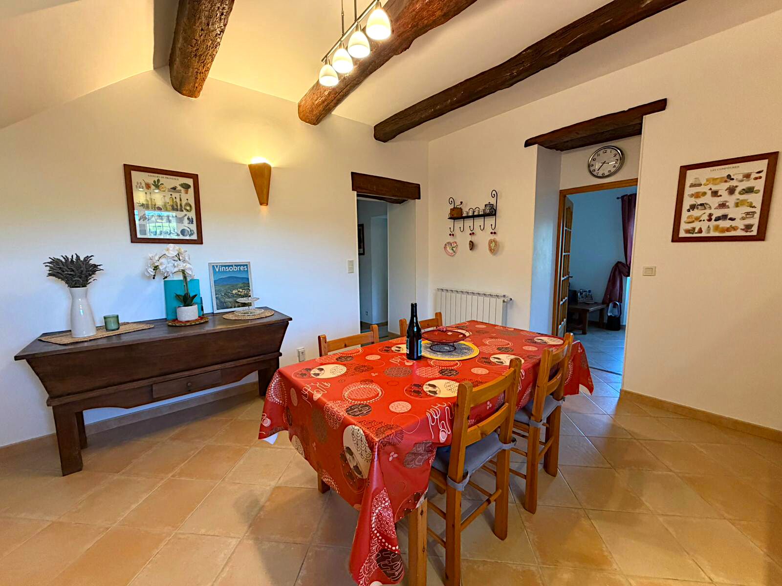 A dining area with a table set for four, a wooden bench, and a wall-mounted clock.