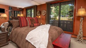 Une chambre avec un grand lit, des lampes de chevet, une table de nuit en bois, un banc rouge et une vue sur l’extérieur grâce à une porte coulissante.