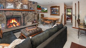 Un salon avec une cheminée en pierre, un canapé, une table à manger avec des chaises et un téléviseur.