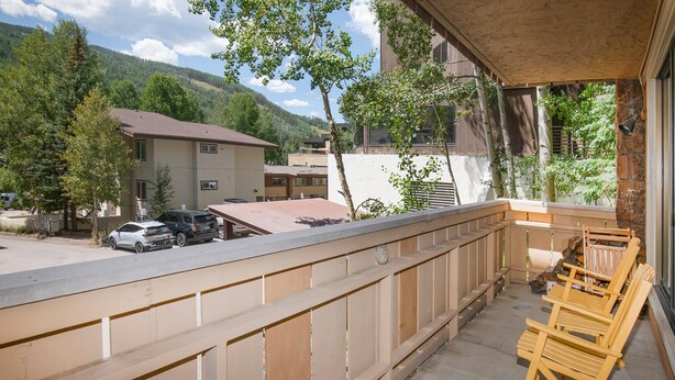 Un balcon doté d’une balustrade en bois, d’un sol en béton et offrant une vue sur une montagne et des bâtiments en arrière-plan.