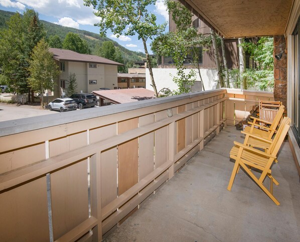A balcony with a wooden railing, a concrete floor, and a view of a mountain and buildings in the background. - Scorpio 101, 2BD Vail Condo With Wood Fireplace (Vail)