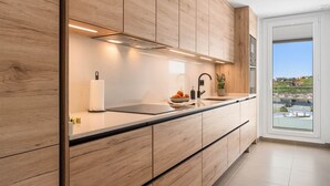 Eine moderne Küche mit Holzschränken, einer schwarzen Arbeitsplatte und Blick auf eine Stadtlandschaft durch ein großes Fenster.