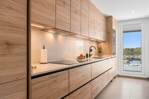Eine moderne Küche mit Holzschränken, einer schwarzen Arbeitsplatte und Blick auf eine Stadtlandschaft durch ein großes Fenster.