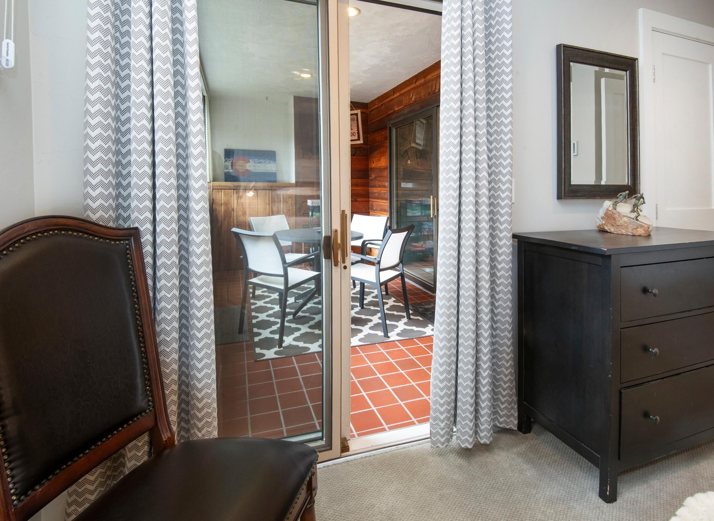 Quarto com porta de vidro deslizante para um pátio, cômoda de madeira escura e uma cadeira.