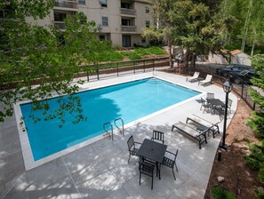 Ein rechteckiger Swimmingpool mit gefliestem Sonnendeck, umgeben von einem Zaun, und Sitzgelegenheiten mit Tischen und Stühlen im Freien.