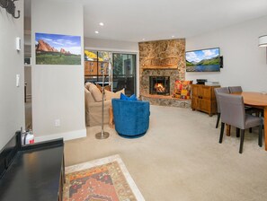 Ein Wohnzimmer mit Kamin aus Stein, einem an der Wand befestigten Fernseher, einem Esstisch mit Stühlen und einem blauen Sessel.