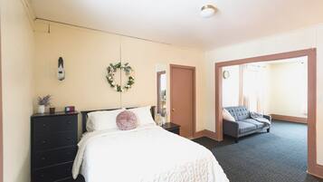 Une chambre à coucher avec un lit, une commode et un canapé gris dans la pièce adjacente.
