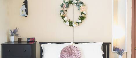 Un dormitorio ordenado con cama, mesita de noche, un reloj de pared, un espejo y una guirnalda decorativa.