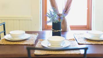 Une table à manger avec deux bols blancs et un vase de fleurs, le tout posé sur des sets de table.