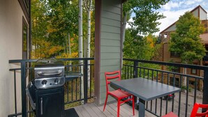 A balcony with a grill, two red chairs, and a table. - Breakaway West 222, 2BD Vail Condo (Vail)
