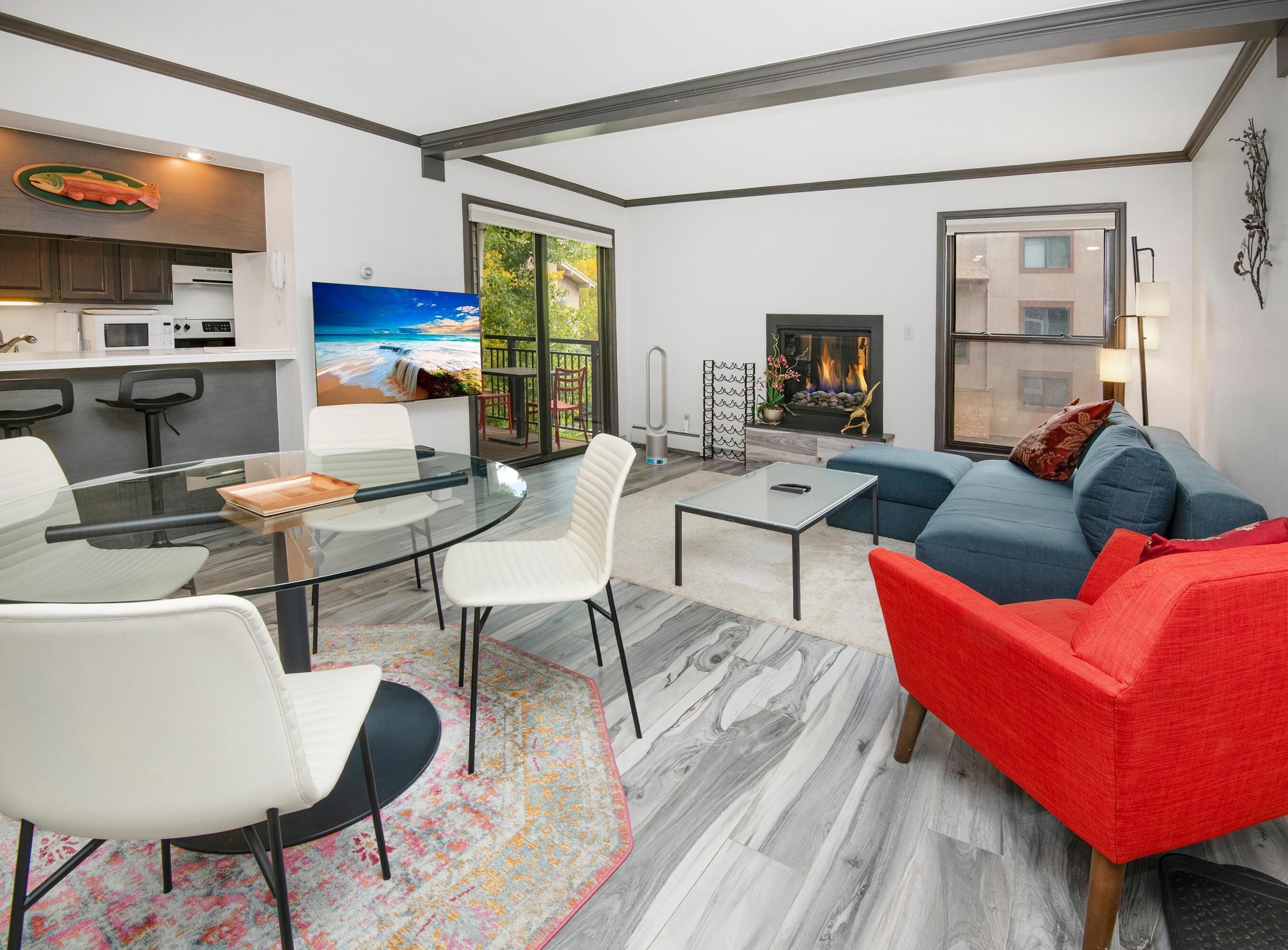 Un salon moderne avec une table à manger en verre, des chaises blanches, un canapé bleu et un fauteuil rouge.