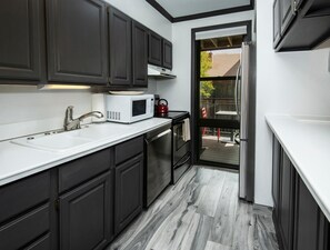 A modern kitchen with dark cabinets, a white countertop, a microwave, a sink, and a view of the outdoors. - Breakaway West 222, 2BD Vail Condo (Vail)