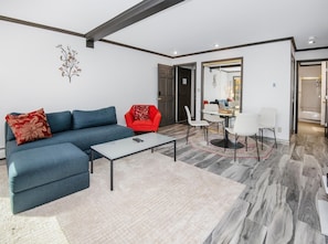 A modern living room with a blue sofa, a red armchair, a glass coffee table, and a dining area with white chairs. - Breakaway West 222, 2BD Vail Condo (Vail)