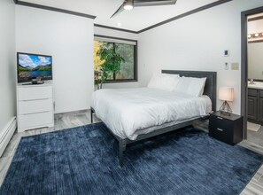A modern bedroom with a bed, a TV, a plant, and a bathroom visible through an open door. - Breakaway West 222, 2BD Vail Condo (Vail)