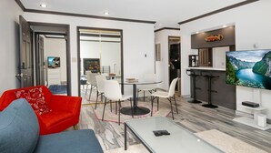 A modern living room with a glass coffee table, a red sofa, a blue sofa, and a dining area with a glass table and white chairs. - Breakaway West 222, 2BD Vail Condo (Vail)