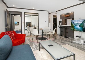 A modern living room with a glass coffee table, a red sofa, a blue sofa, and a dining area with a glass table and white chairs. - Breakaway West 222, 2BD Vail Condo (Vail)