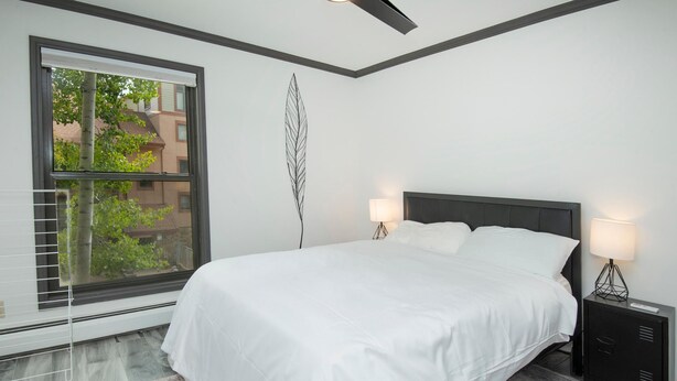 A bedroom with a large bed, two bedside tables with lamps, a window with blinds, and a patterned rug. - Breakaway West 222, 2BD Vail Condo (Vail)