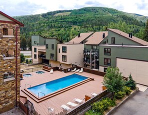 A residential building with a swimming pool, outdoor seating, and a view of a forested mountain. - Breakaway West 222, 2BD Vail Condo (Vail)
