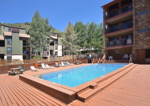 A pool area with lounge chairs, a wooden deck, and a building with multiple balconies. - Breakaway West 222, 2BD Vail Condo (Vail)