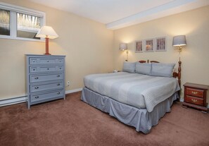 Ein Schlafzimmer mit Bett, Schminktisch, Nachttisch, Lampe und Wandbildern.