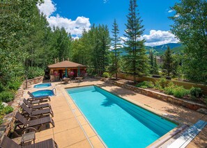 Ein Pool mit Liegestühlen, eine kleine Laube und ein Bergpanorama im Hintergrund.