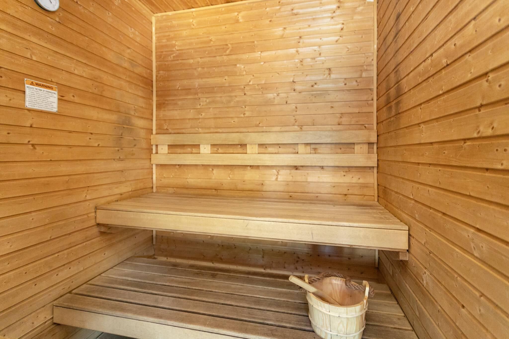 Een houten sauna met banken, een houten zitting en een emmer.
