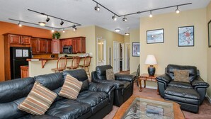 A living room with a black leather sofa, a glass coffee table, and a leather armchair. There is a kitchen area with wooden cabinets and a microwave. - Sun Vail 12e, 2BD Condo With Vail Mountain Views (Vail)