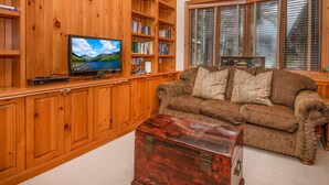 Ein Wohnzimmer mit Holzwand, Fernseher, Bücherregal, braunem Sofa und einer Holzablage.