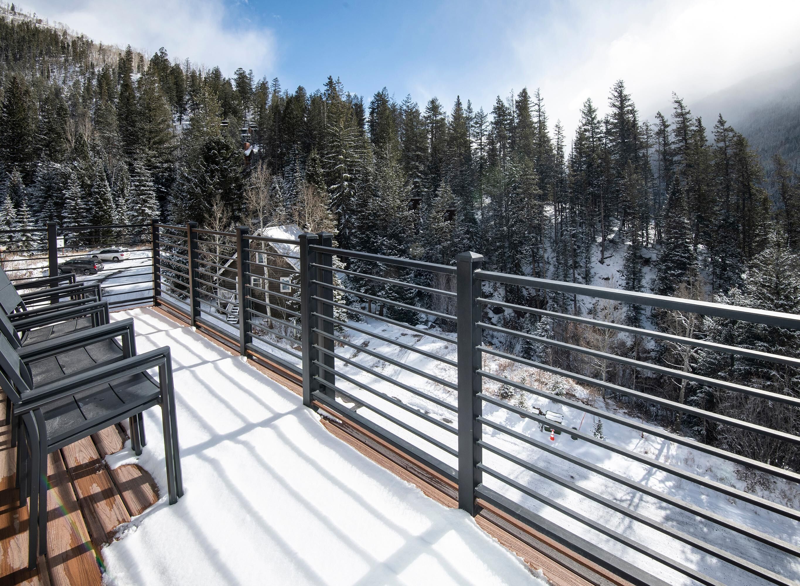 A snow-covered deck with a railing overlooking a forested mountain area.
