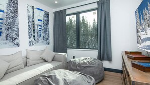 Ein modernes Wohnzimmer mit einer Couch, zwei Sitzsäcken, einem Holztisch mit Büchern und einem Fenster mit Blick auf schneebedeckte Bäume.