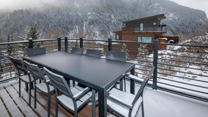 Ein Essbereich mit Tisch und Stühlen auf einer Terrasse, mit Blick auf eine Berglandschaft.