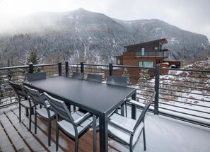 Ein Essbereich mit Tisch und Stühlen auf einer Terrasse, mit Blick auf eine Berglandschaft.