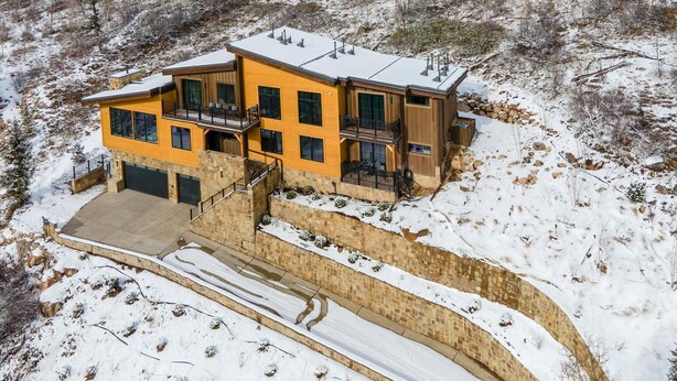 Ein modernes, zweistöckiges Haus mit einer Steinmauer, einer überdachten Auffahrt und verschneiter Landschaft.