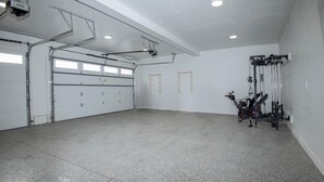 Eine geräumige Garage mit Betonboden, einem an der Decke befestigten Projektor und einem an der Wand montierten Fitnessgerät.