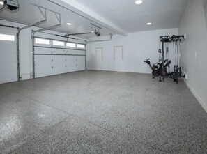 Eine geräumige Garage mit Betonboden, einem an der Decke befestigten Projektor und einem an der Wand montierten Fitnessgerät.